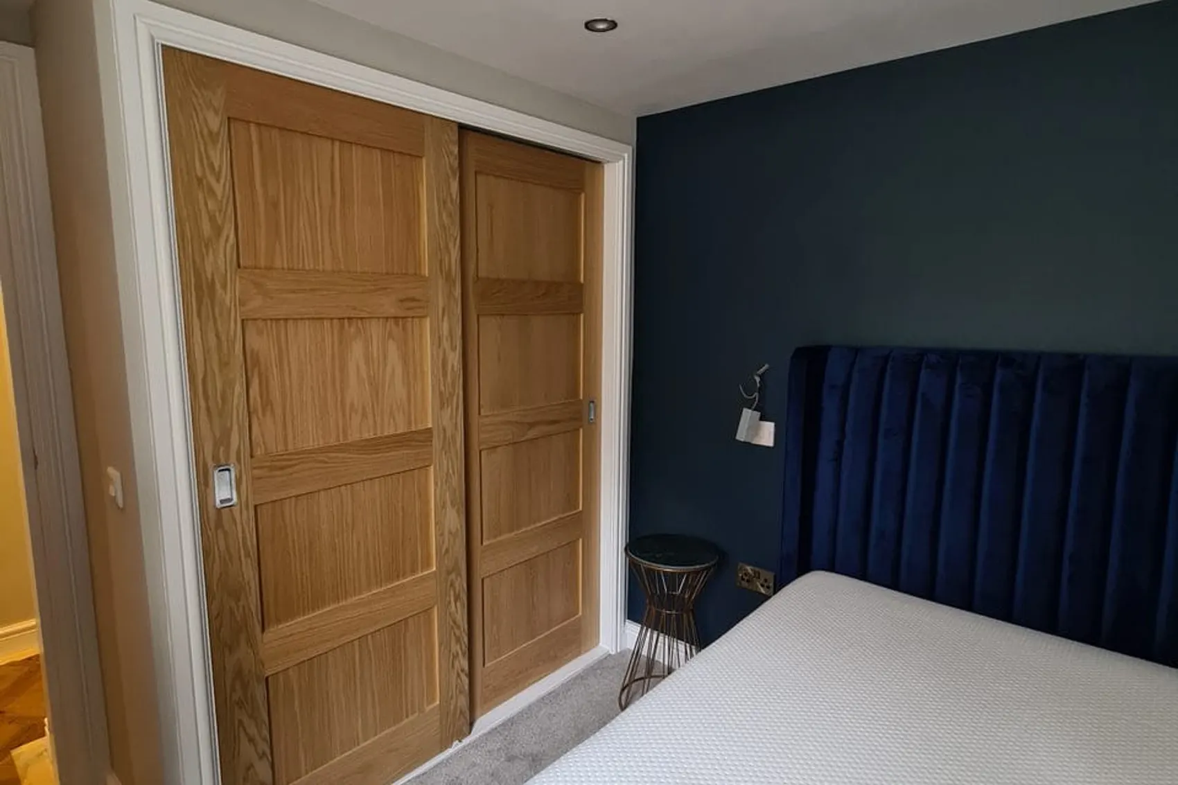 Bedroom with fitted sliding oak wardrobes and a navy feature wall, renovated by Abbey Group