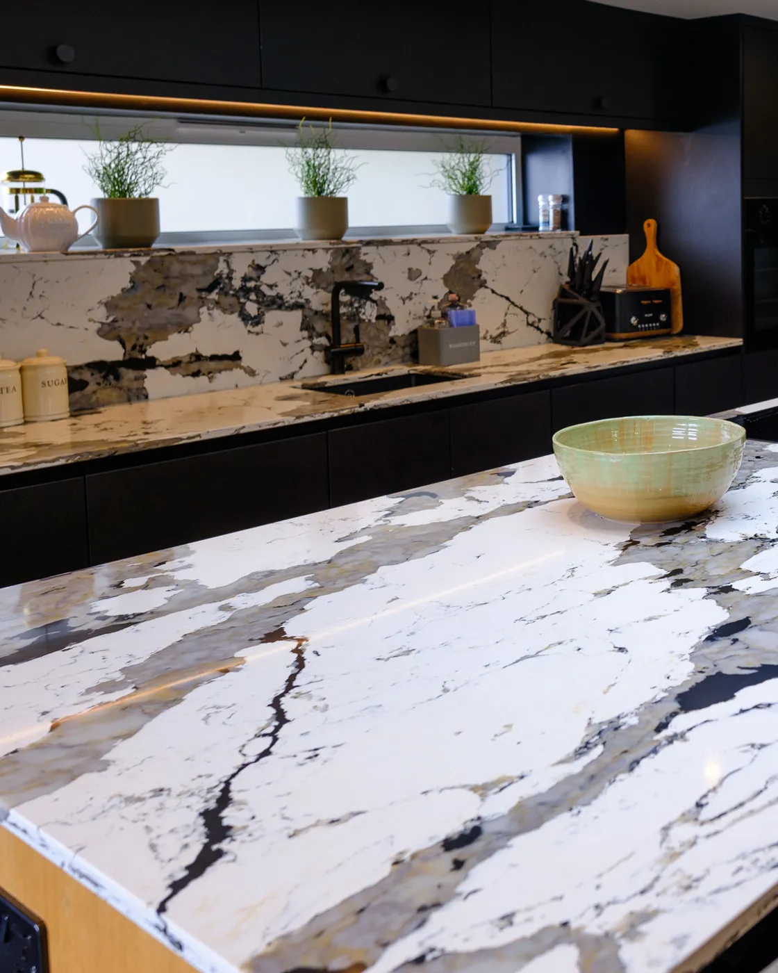 Bespoke kitchen with black handleless units and a book-matched quartz island, renovated by Abbey Group