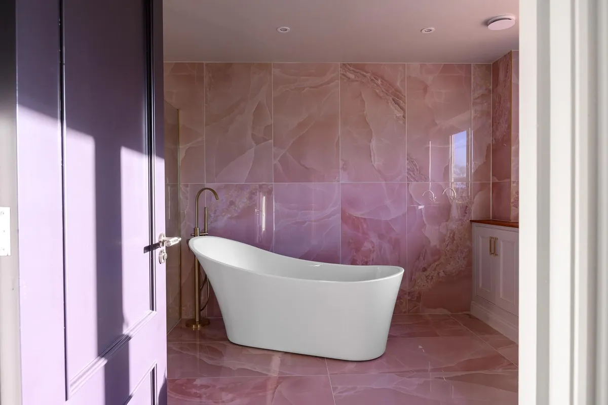 Bathroom with pink onyx marble walls, a freestanding bath and brushed brass fittings by Abbey Group